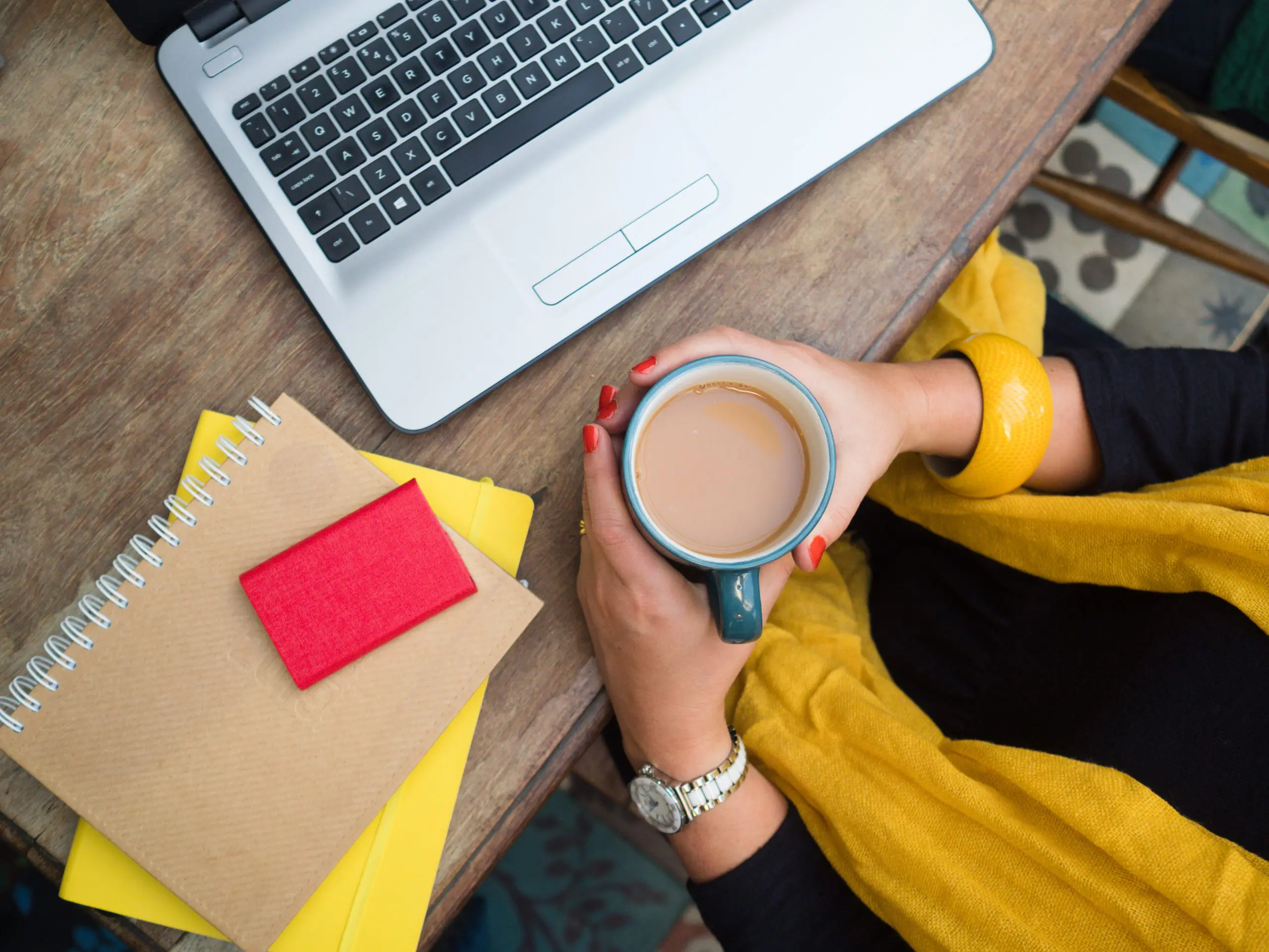 turning-setbacks-into-strategy-financial-recovery-guide Woman holding a coffee cup at a desk with a laptop and notebooks, symbolising reflection and planning after financial challenges.